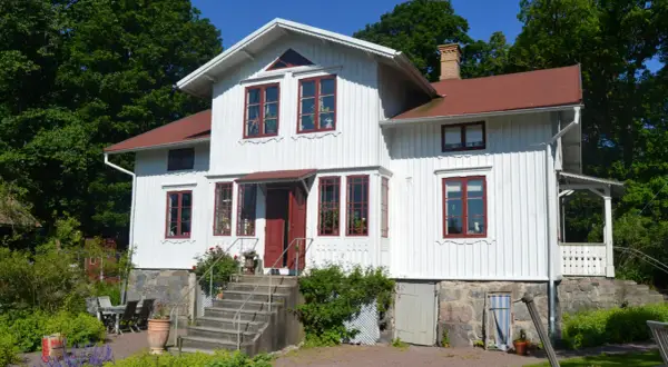 Vitt trähus med röda fönster och tak, en vacker **midja på gammalt hus** omgiven av grönskande träd.