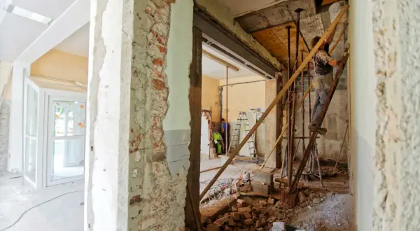 Renovering av ett sekelskiftes hus. Byggnadsställningar, rivningsmaterial och arbetare syns i det pågående arbetet.