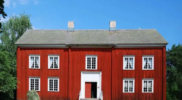 Rött trähus med vita fönster och skorstenar. En höstack ligger framför. Tänk på ventilation i gamla hus när du ser detta.
