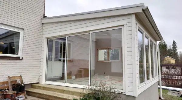 Ett modernt hus med glasveranda, med stora skjutdörrar i glas som släpper in mycket ljus. Trädäck och trappa leder upp till verandan.