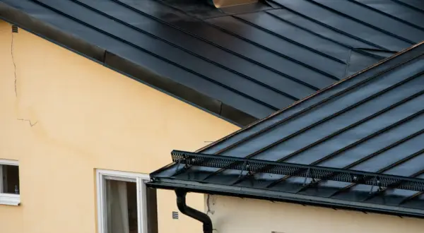 Detaljerad vy av en mörk plåttak konstruktion över ett gult hus med fönster.