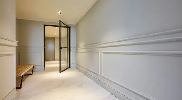 Elegant hall med stuckatur och marmorgolv. En öppen glasdörr leder in till ett ljust rum.