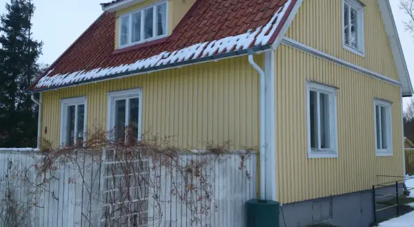 Gult 40-talshus med tegeltak och snö på takfoten. Ett staket med klätterväxter löper framför huset. Planer på att renovera 40-talshus?