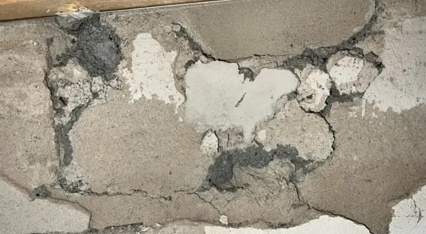 Skadad vägg med mörkgrå, smulig massa som kan vara blåbetong med asbest. Sprickor och avskalningar syns tydligt.
