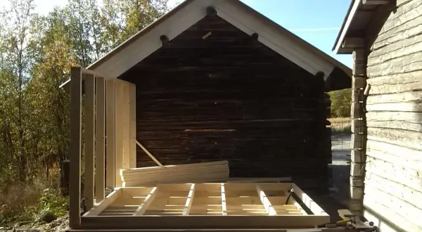 Bygga ut timmerhus. Ny stomme reses vid ett gammalt timrat hus.