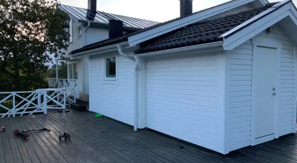 Vitt hus med mörk takläggning, en del av taket är under utbyggnad. Två sparkcyklar ligger på altanen.