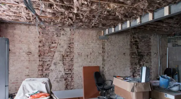 Bygga om hus: synliga bjälkar, isolering och tegelväggar vittnar om renovering. Material och verktyg ligger utspridda.