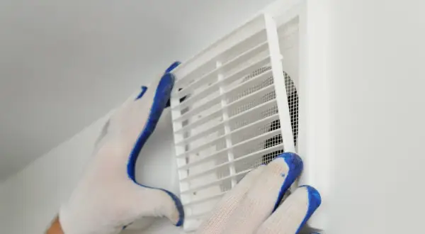Händer med handskar rengör ett ventilationsgaller för att förbättra dammigt hemma ventilation.