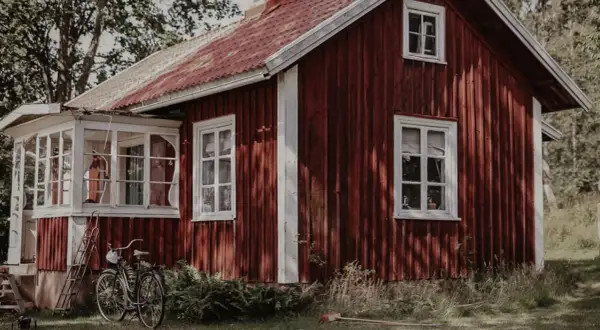 Rött torp med vit veranda och en cykel parkerad utanför. En idyllisk svensk sommaridyll.