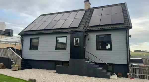 A light gray house with solar panels on the roof and a brick chimney.