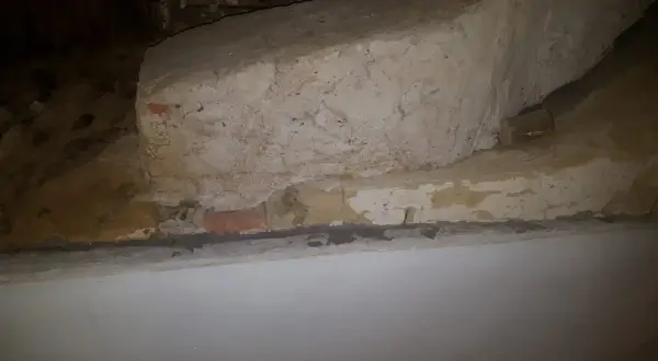 Detaljerad vy av en gammal murstock som är i behov av att riva murstock. Synliga tegelstenar och puts.