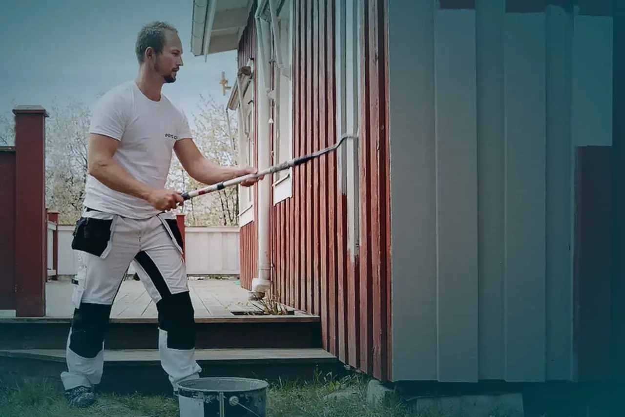 Ett tegelhus med en tillbyggnad i mörk träpanel under ett tegeltak. Uteplats med möbler och grönskande trädgård.
