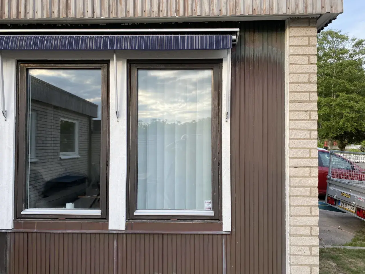 Två fönster med mörkbrun karm och en randig markis ovanför. En ny fasad utanpå den gamla, med träpanel och tegel.
