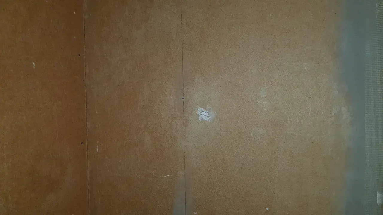 En vägg av masonit där man börjat måla. En vertikal linje syns i mitten, och lite vitt pulver på ytan.