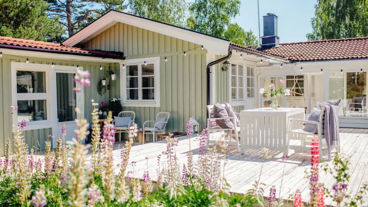 Ett charmigt hus med ljusgröna väggar, perfekt för att måla huset i sommar. Trädäck med vita möbler och blommor.