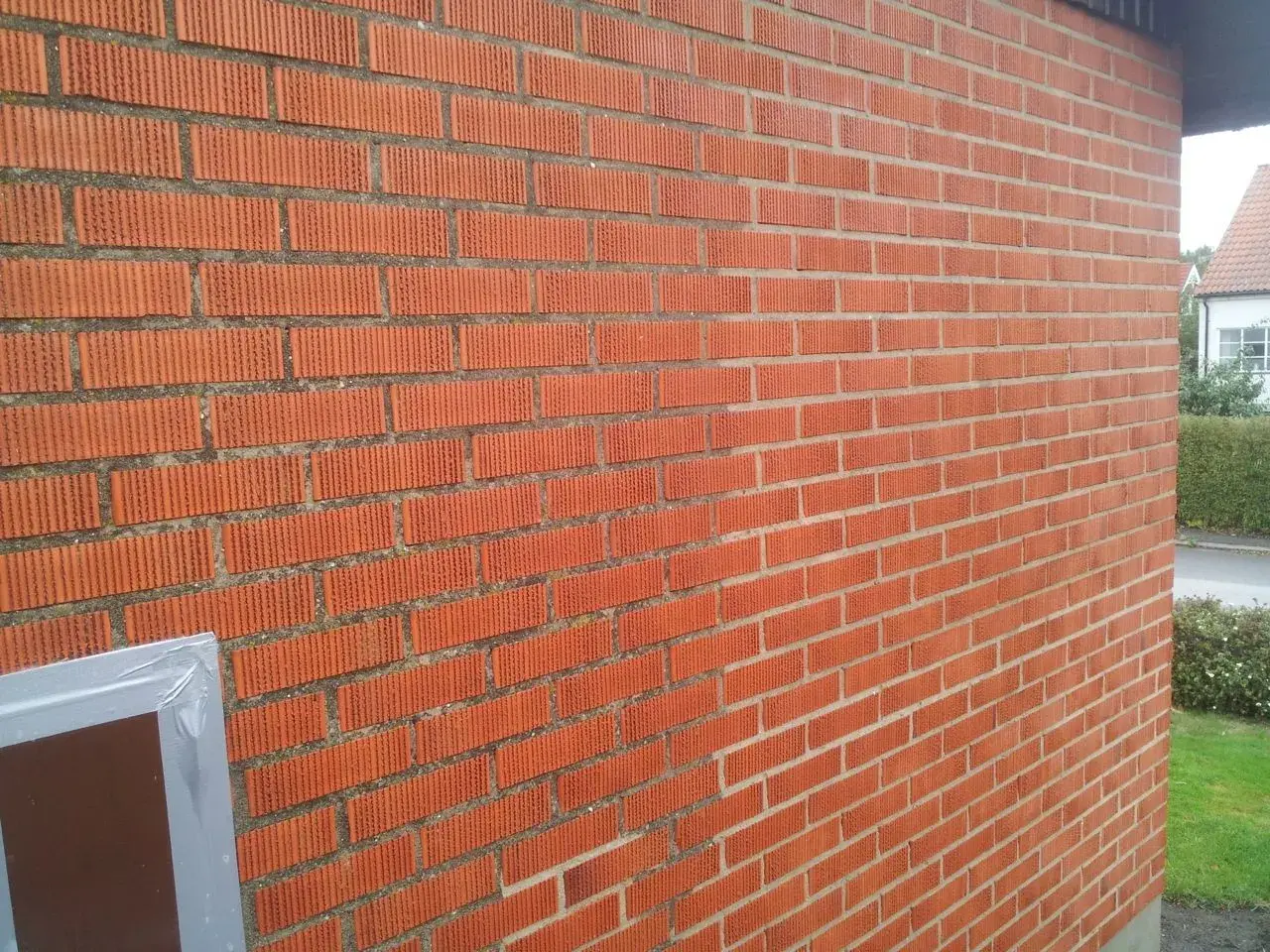 En röd tegelfasad med vertikala spår i tegelstenarna. En del av en fönsterkarm syns i nedre vänstra hörnet.