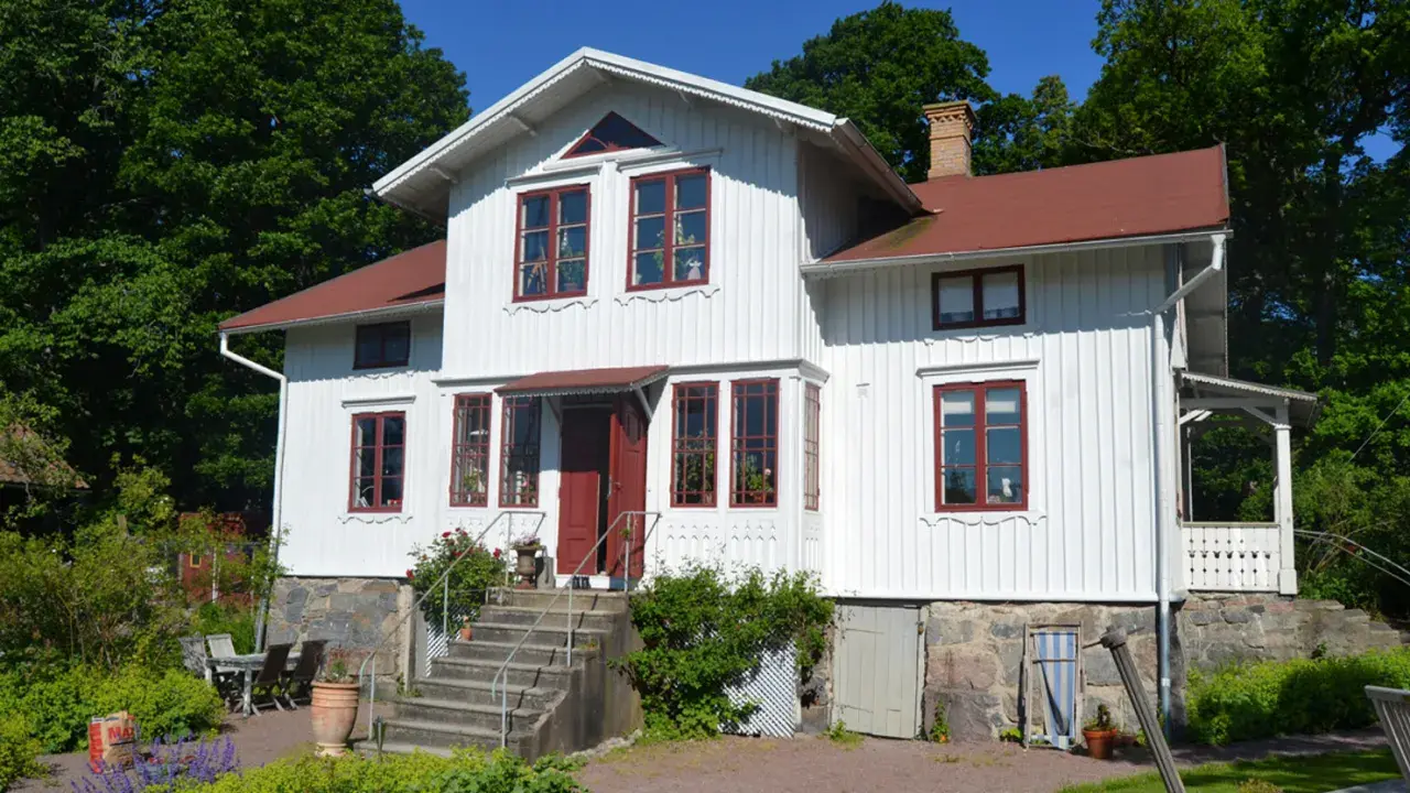 Vitt trähus med röda fönster och tak, en vacker **midja på gammalt hus** omgiven av grönskande träd.