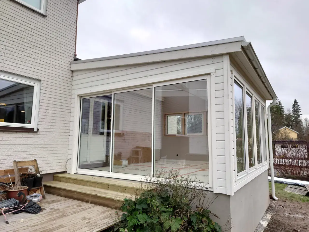 Ett modernt hus med glasveranda, med stora skjutdörrar i glas som släpper in mycket ljus. Trädäck och trappa leder upp till verandan.
