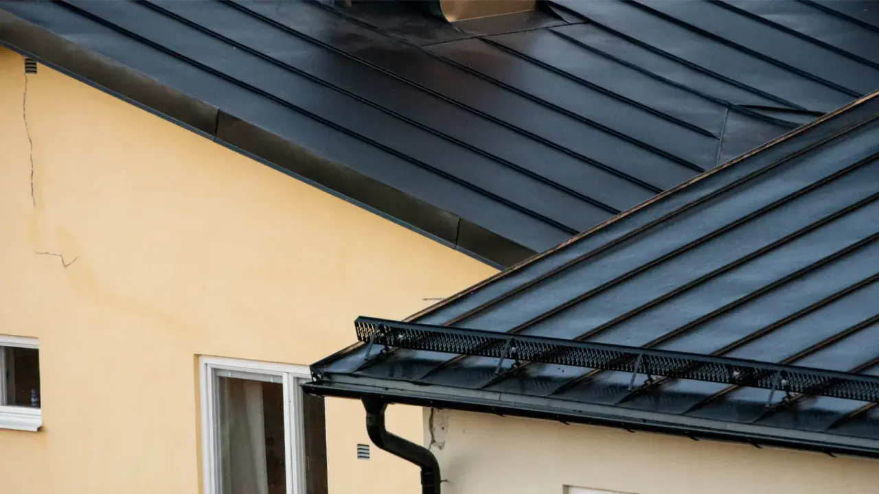 Detaljerad vy av en mörk plåttak konstruktion över ett gult hus med fönster.