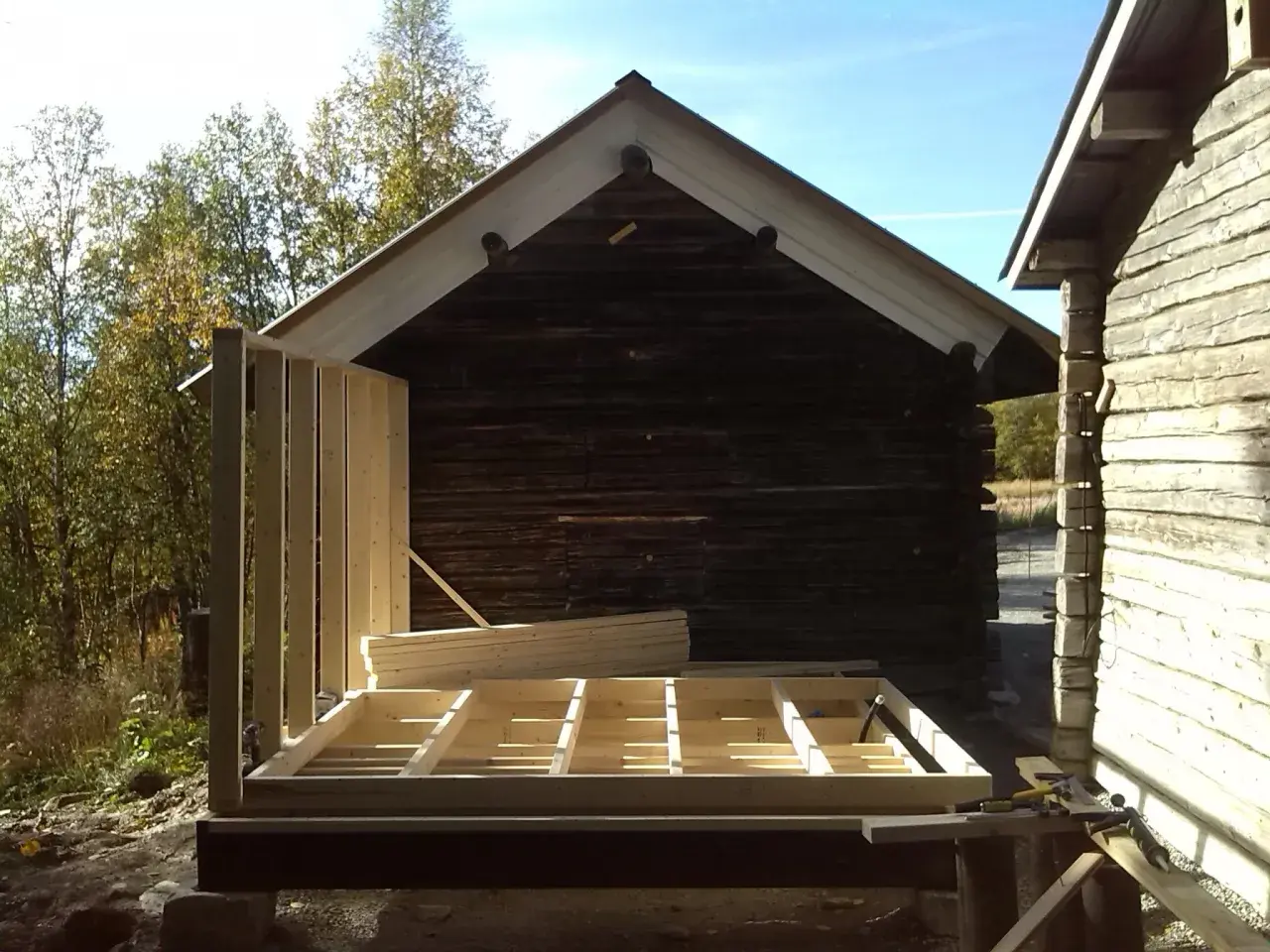 Bygga ut timmerhus. Ny stomme reses vid ett gammalt timrat hus.