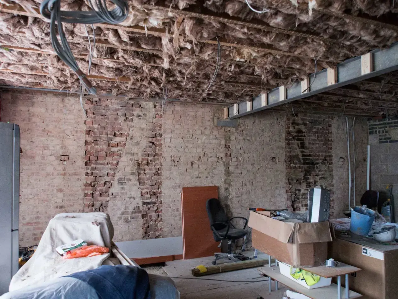 Bygga om hus: synliga bjälkar, isolering och tegelväggar vittnar om renovering. Material och verktyg ligger utspridda.