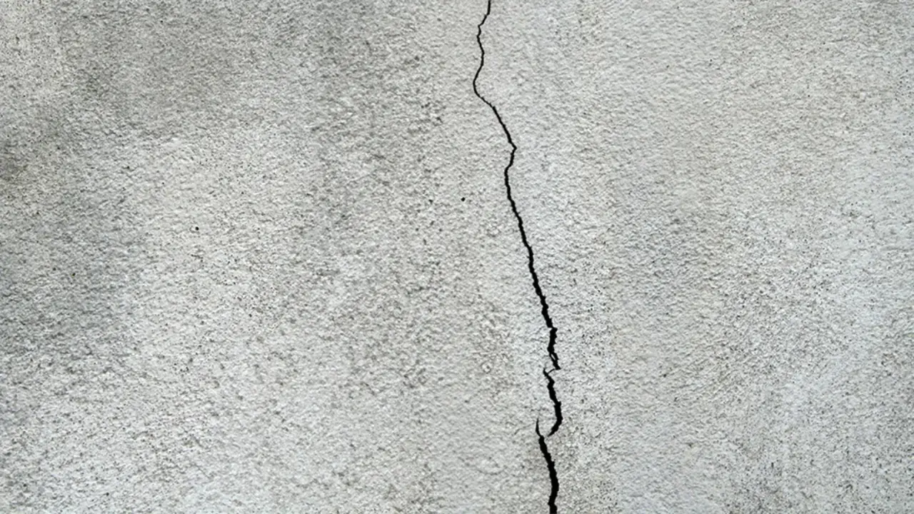 En spricka löper genom en grå, putsad fasad. Dags att laga sprickor i putsad fasad för att skydda huset.
