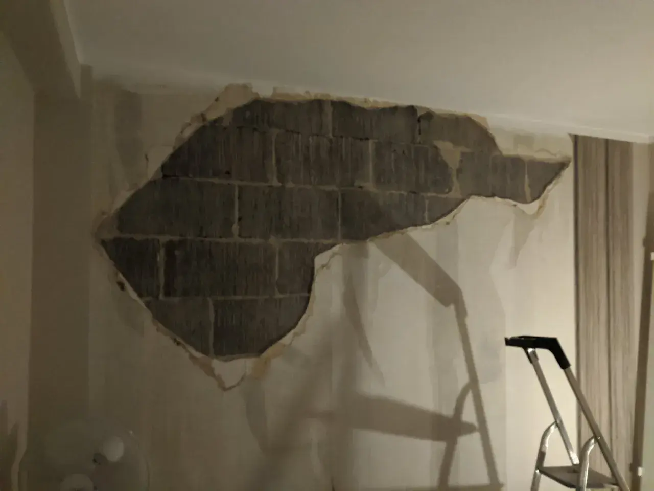 Stor fläck av puts som lossnat från en tegelvägg inomhus. En stege står redo för att laga puts inomhus.