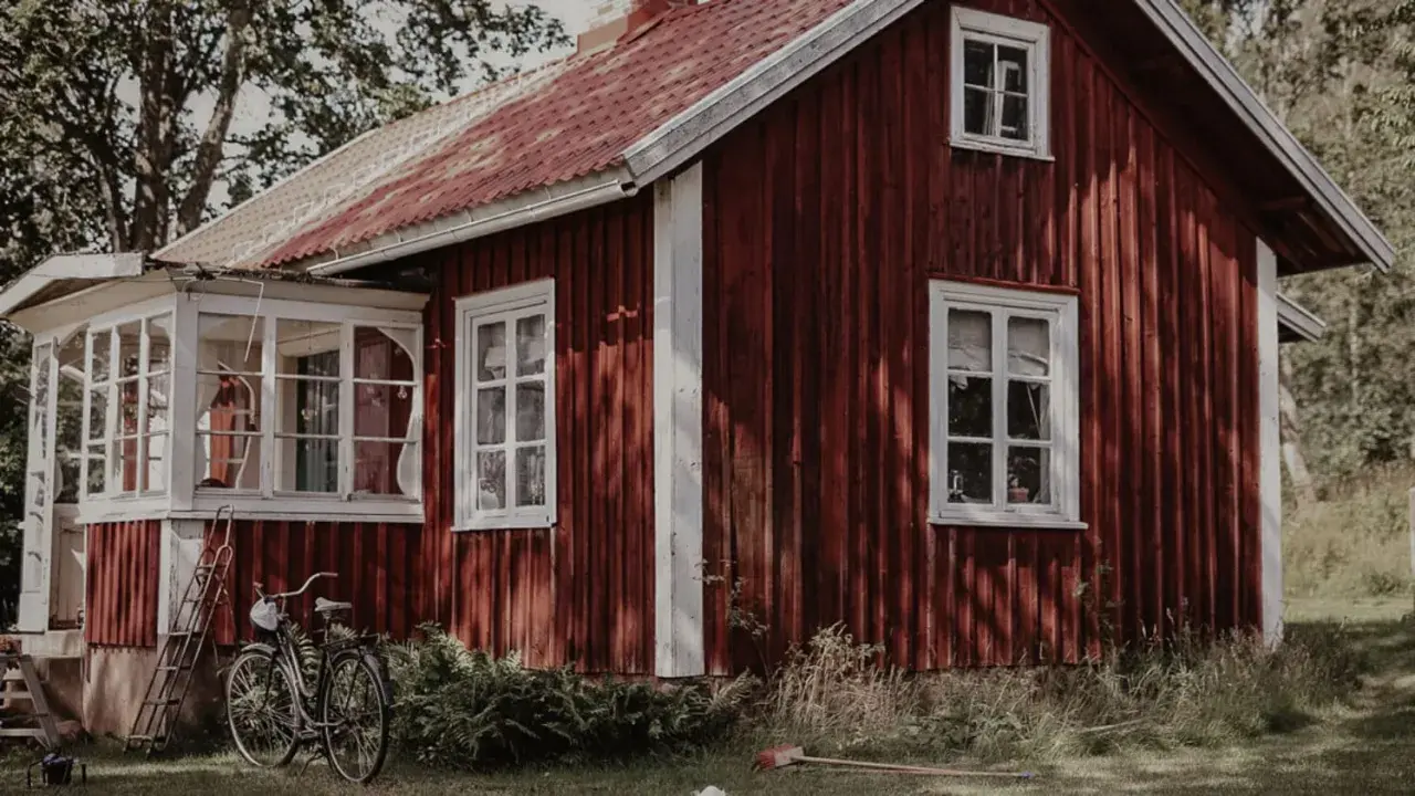 Rött torp med vit veranda och en cykel parkerad utanför. En idyllisk svensk sommaridyll.