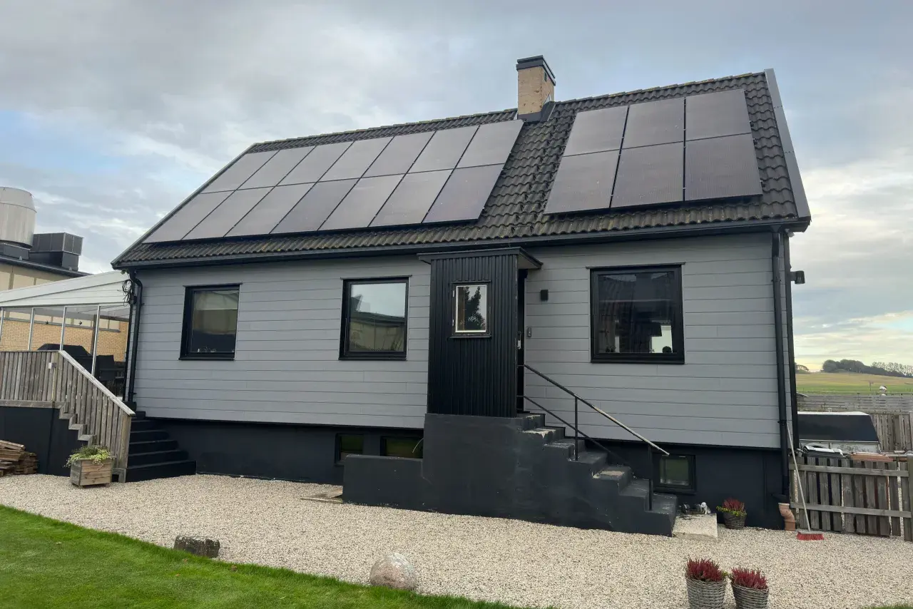 A light gray house with solar panels on the roof and a brick chimney.