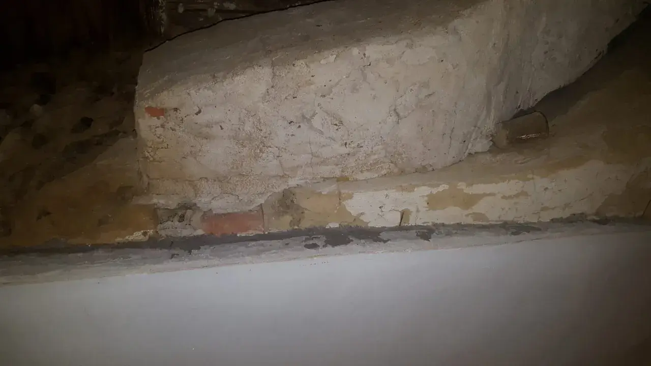 Detaljerad vy av en gammal murstock som är i behov av att riva murstock. Synliga tegelstenar och puts.