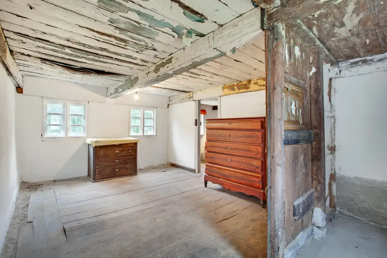 Ett rum i ett hus från 1700-talet med slitna trägolv, takbjälkar och två gamla byråer.