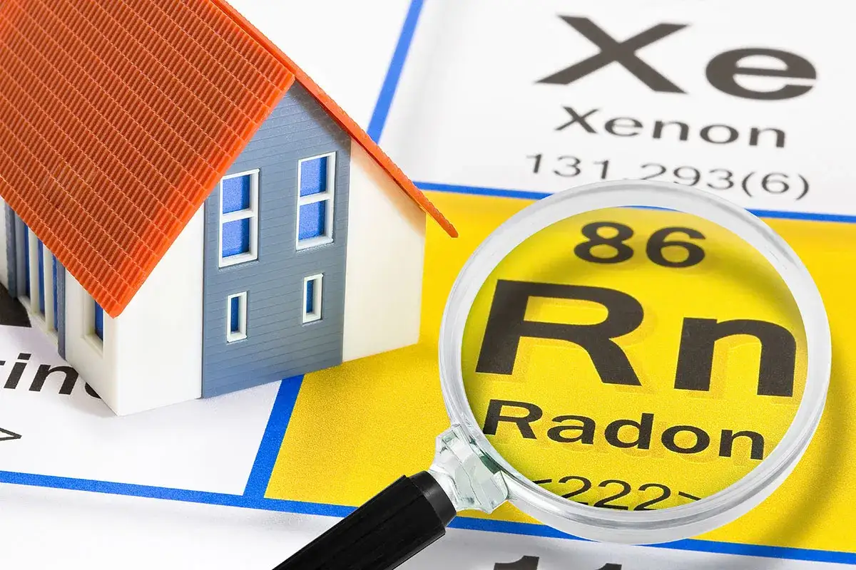 En modell av ett hus undersöks med ett förstoringsglas som visar grundämnet radon.