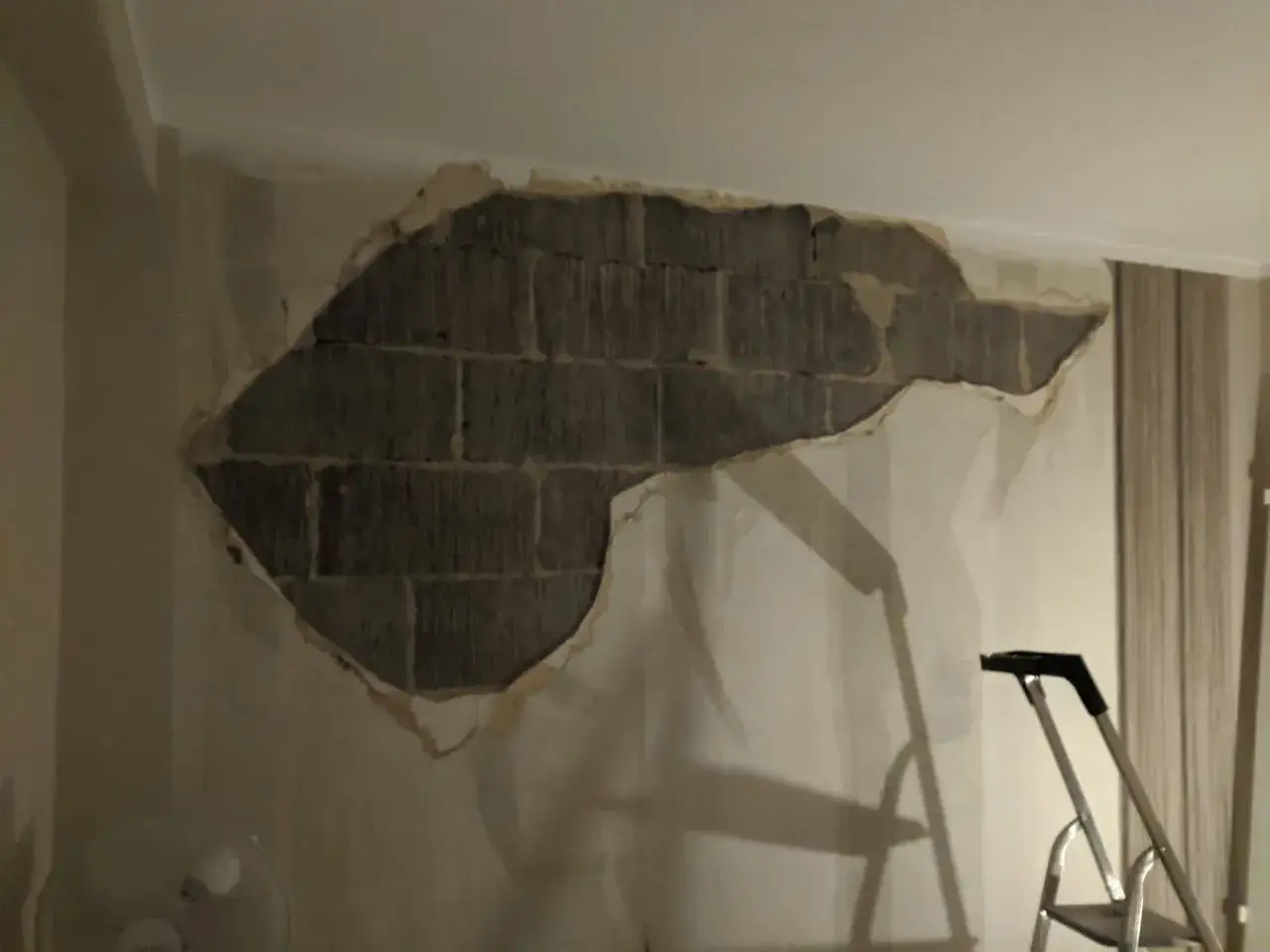 En stor del av tapeten har lossnat och blottar en tegelvägg. En stege står redo för att laga puts inomhus.