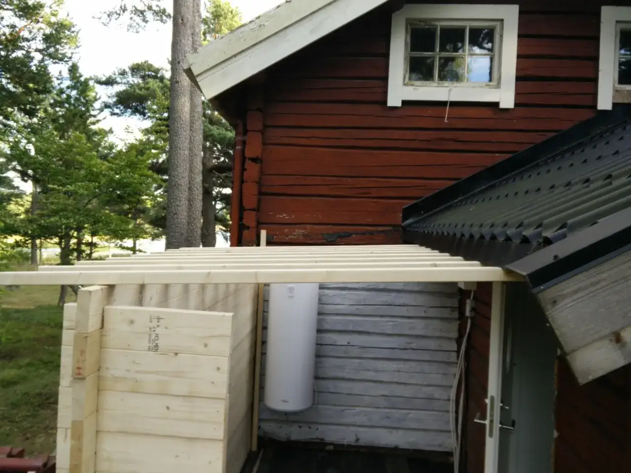 Nybyggd tillbyggnad med takanslutning mot r&ouml;tt tr&auml;hus. Vattenberedare syns p&aring; v&auml;ggen.