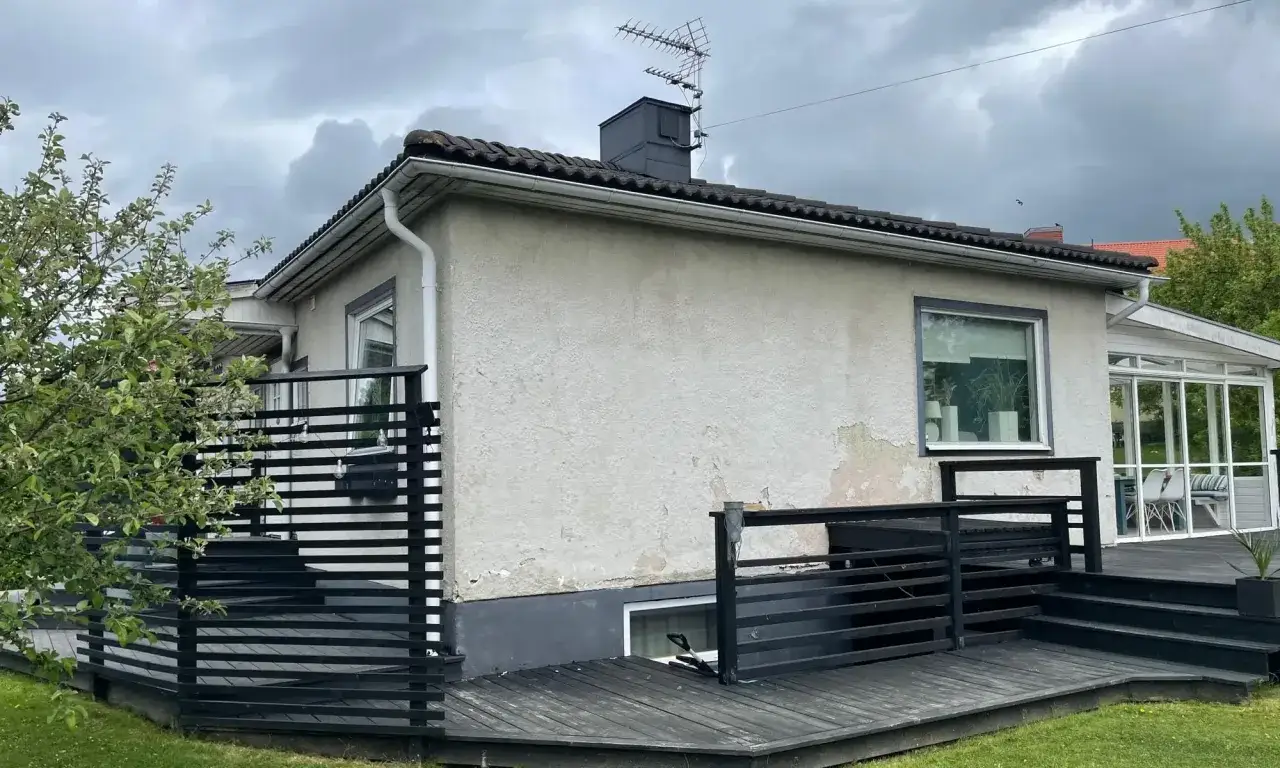 Ett hus med gr&aring; putsad fasad och en svart tr&auml;altan. En antenn syns p&aring; taket.