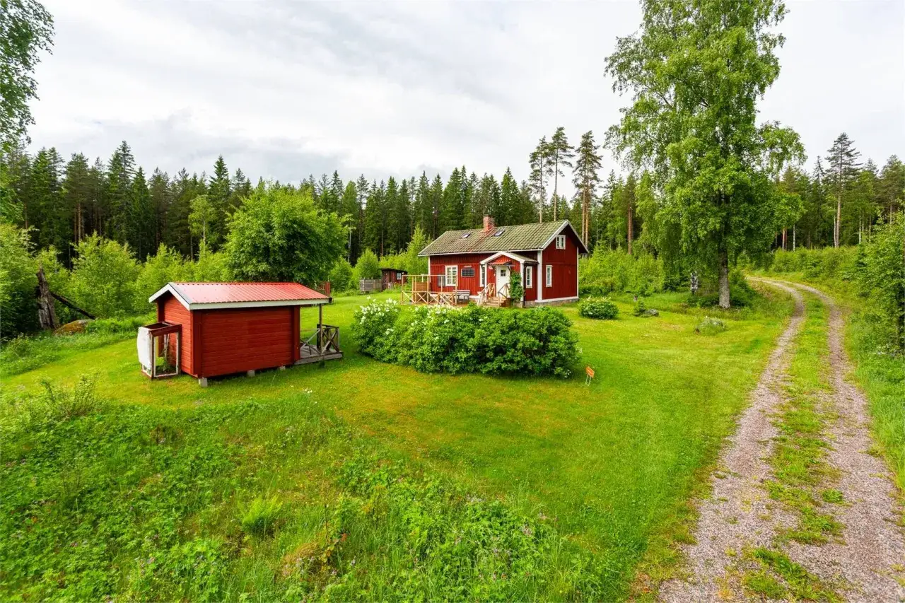 Rött hus med vita knutar och en mindre röd bod i en grönskande trädgård. Kanske ett av de billigaste husen i Sverige?