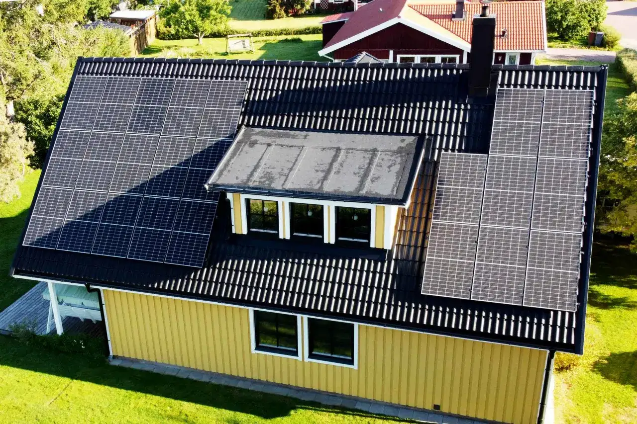 Gult hus med svart tak t&auml;ckt av solpaneler. Ett modernt hem som f&aring;ngar solens energi.