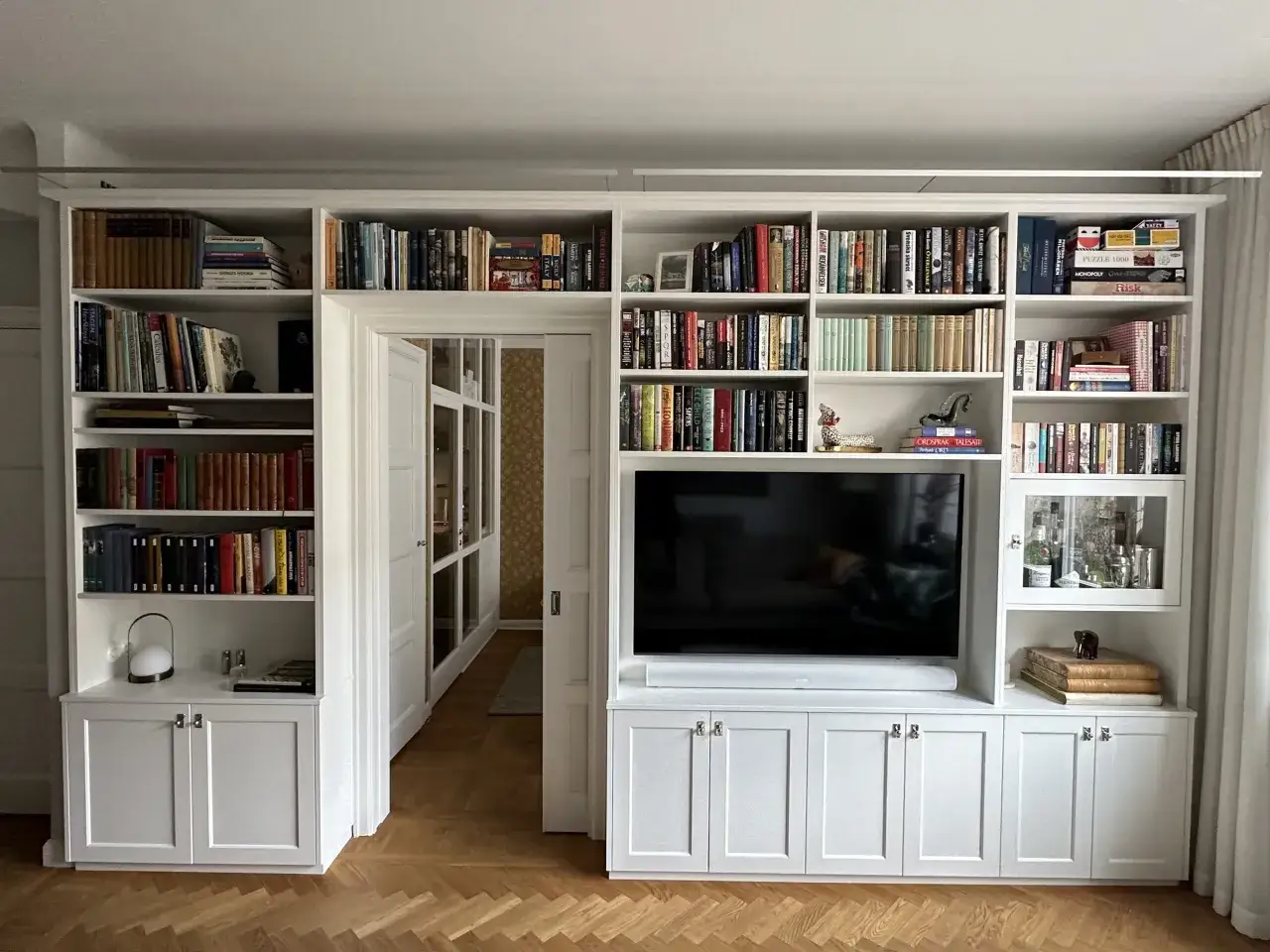 Vit platsbyggd bokhylla med TV, böcker och förvaring. Pris för en sådan platsbyggd bokhylla kan variera.