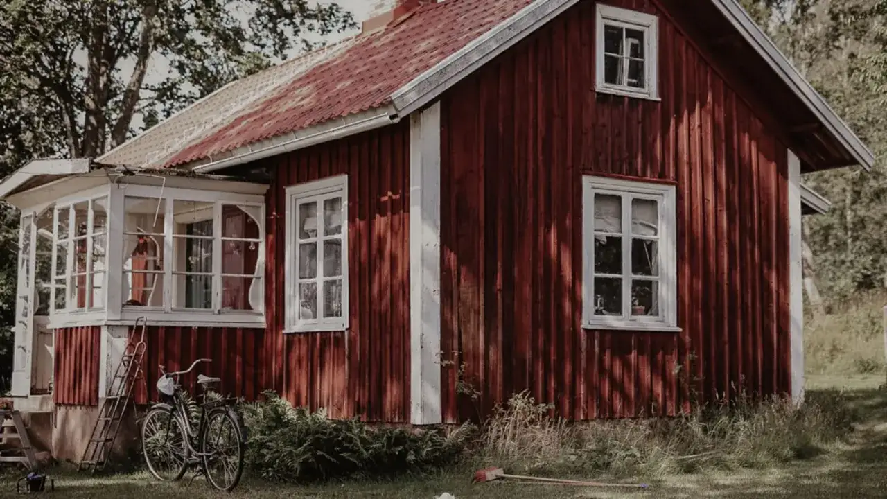 R&ouml;tt torp med veranda och en cykel utanf&ouml;r. Solen lyser p&aring; den gamla tr&auml;fasaden.