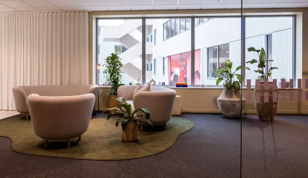 Mjukt inredd kontorsyta med bekväma sittmöbler och gröna växter. En inspirerande miljö som kan påverka byggkostnad per kvadratmeter kontor.