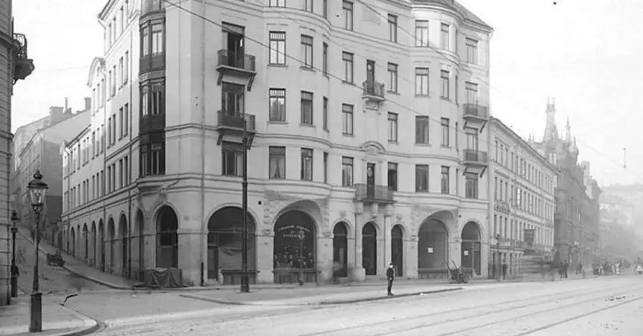 Ett ståtligt jugendstil hus med rundade hörn och balkonger. En man står på trottoaren framför byggnaden.