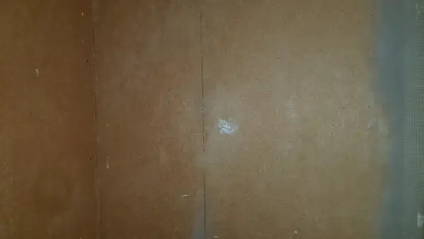 En vägg av masonit där man börjat måla. En vertikal linje syns i mitten, och lite vitt pulver på ytan.