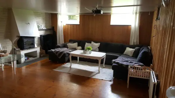 En mysig gillestuga med stor soffa, öppen spis och träpaneler. Perfekt för att renovera gillestuga till ett modernt allrum.