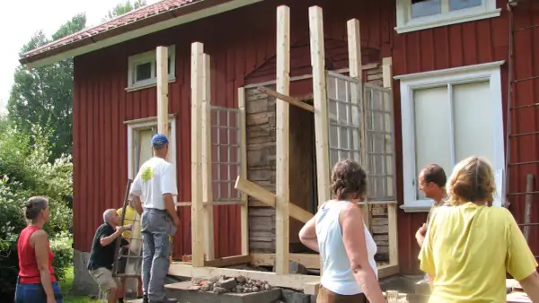 Byggnation av glasveranda entre. Människor hjälps åt att bygga en ny entré med gamla fönster.