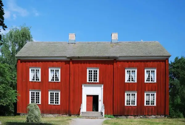 Rött trähus med vita fönster och skorstenar. En höstack ligger framför. Tänk på ventilation i gamla hus när du ser detta.