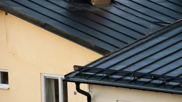 Detaljerad vy av en mörk plåttak konstruktion över ett gult hus med fönster.