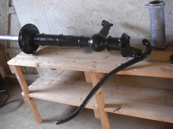 Svartmålad gårdspump, redo för renovering. Den ligger på en träbänk i ett garage.