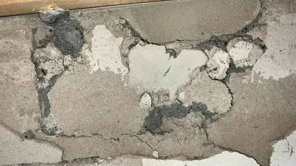 Skadad vägg med mörkgrå, smulig massa som kan vara blåbetong med asbest. Sprickor och avskalningar syns tydligt.