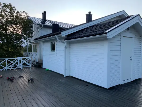 Vitt hus med mörk takläggning, en del av taket är under utbyggnad. Två sparkcyklar ligger på altanen.