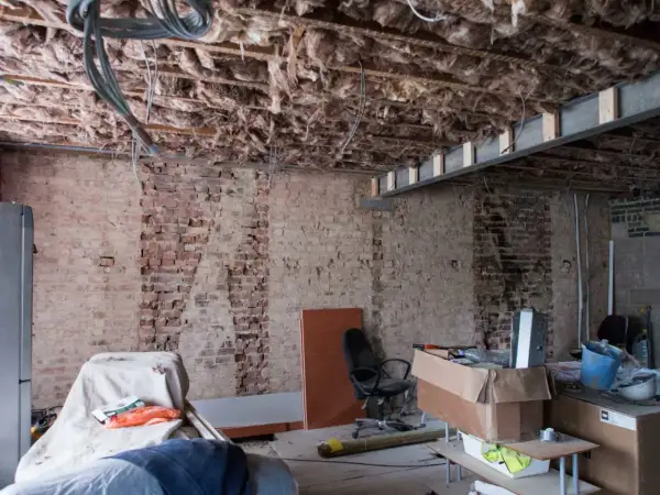 Bygga om hus: synliga bjälkar, isolering och tegelväggar vittnar om renovering. Material och verktyg ligger utspridda.